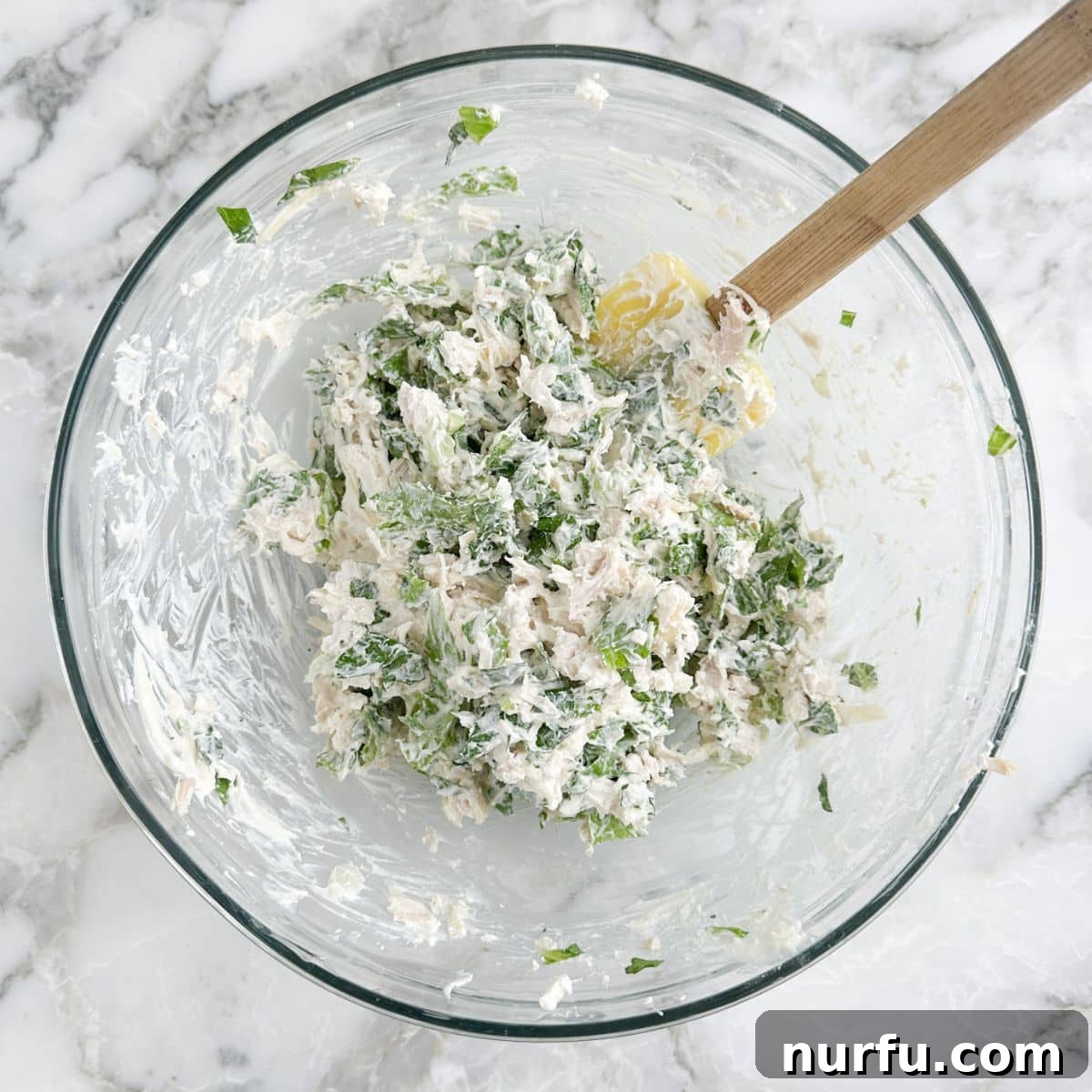 A bowl filled with the complete chicken Caesar salad mixture, ready for spreading onto tortillas.