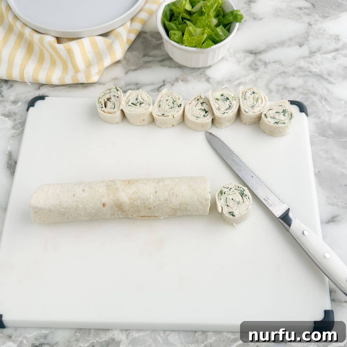 A sharp knife slicing through a chilled chicken Caesar pinwheel roll, creating neat, bite-sized pieces.
