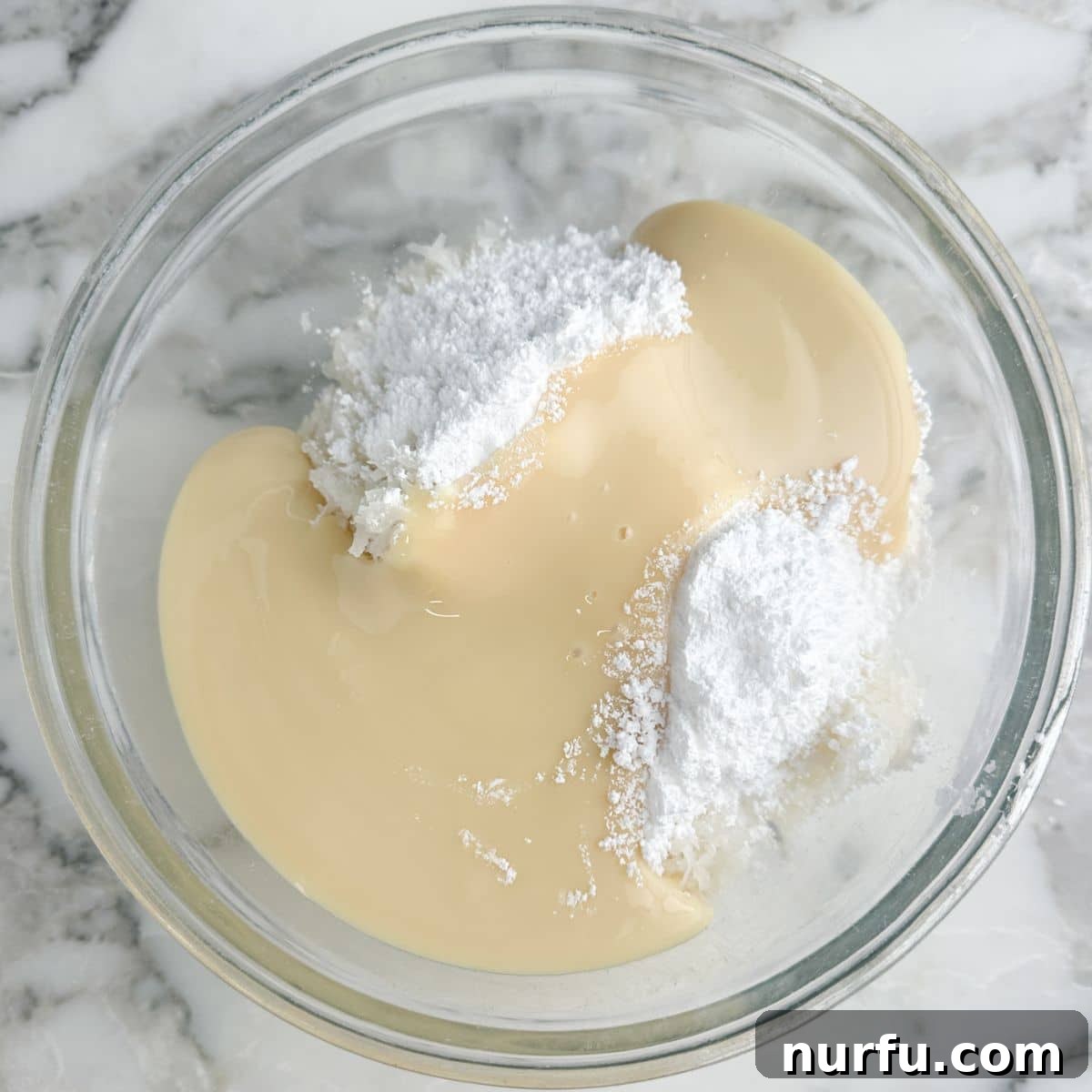 A glass bowl filled with the sweet coconut mixture, featuring shredded coconut, sweetened condensed milk, and powdered sugar, ready to be spread.
