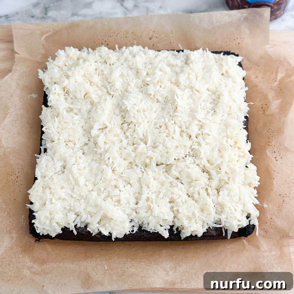 A freshly baked pan of brownies, now completely cooled, expertly topped with an even layer of the sweet, white shredded coconut mixture.