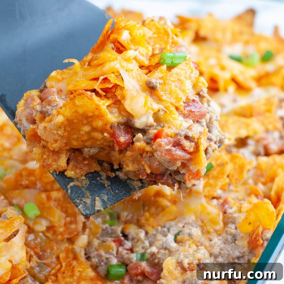 Scoop of Doritos casserole, showcasing layers of beef, cheese, and crunchy chips.