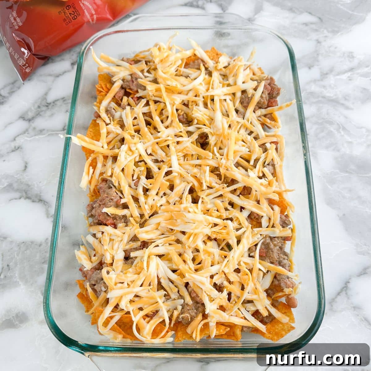 Casserole dish with a layer of Doritos chips, followed by ground beef and shredded cheese.