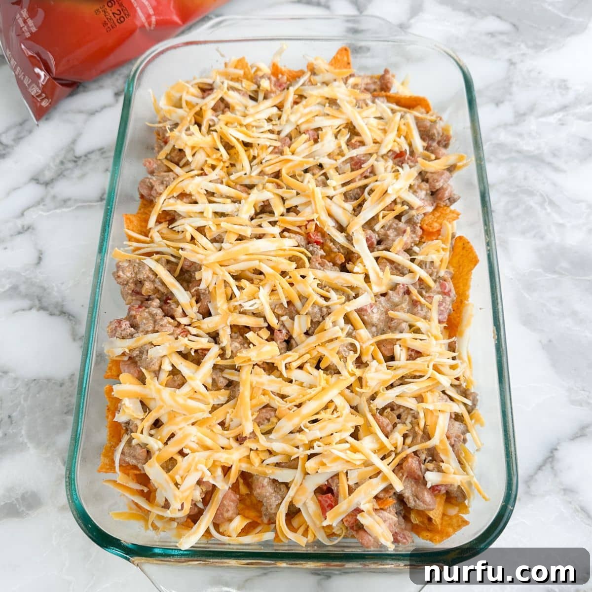 Casserole dish with more Doritos chips, ground beef, and shredded cheese, building up the layers.