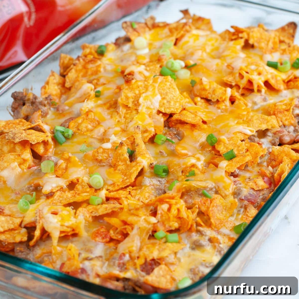 Casserole dish with baked Doritos casserole, topped with fresh garnishes.