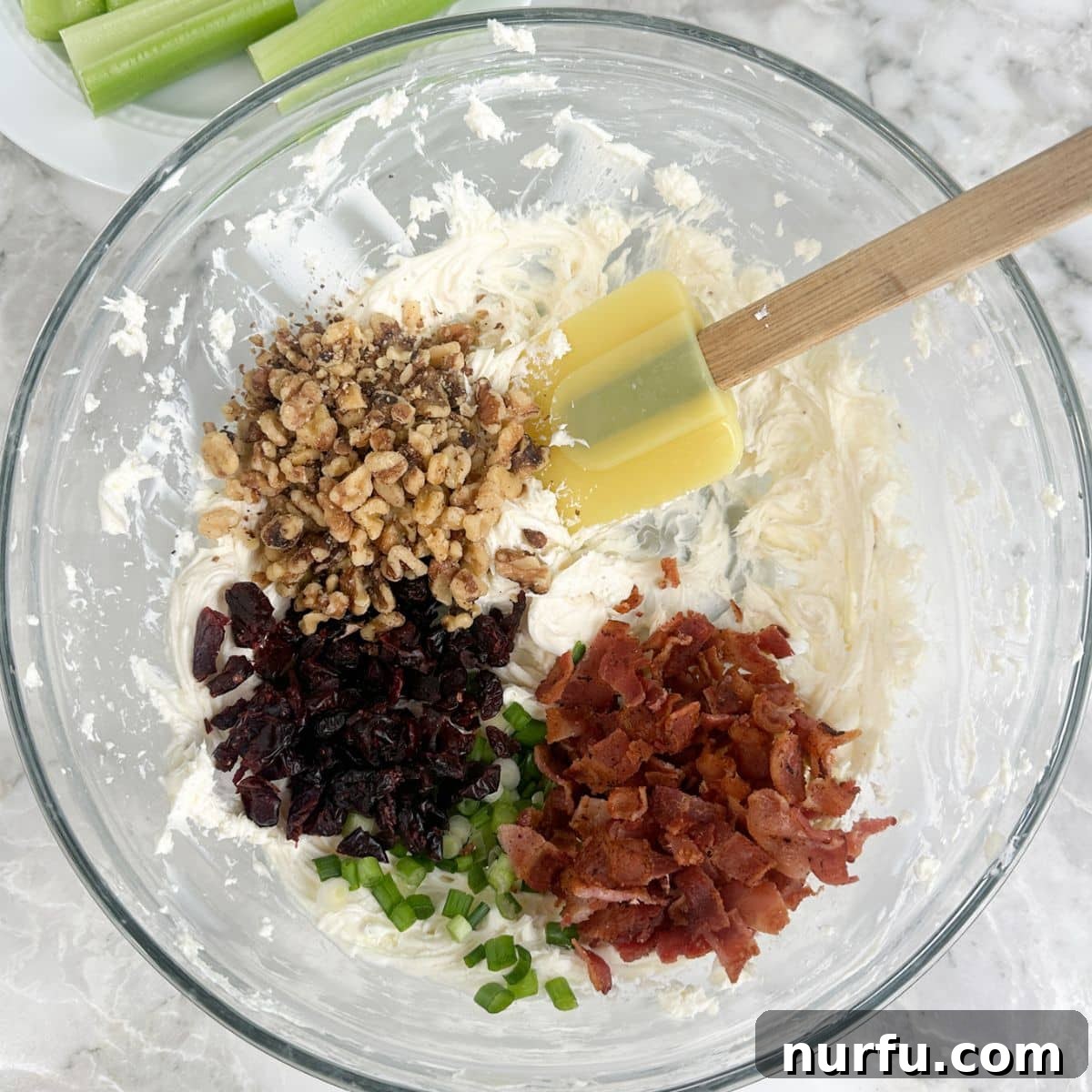 Creamy Celery Crunch 5 A bowl showcasing the whipped cream cheese mixture, now enhanced with finely chopped walnuts, crispy bacon bits, and vibrant dried cranberries, awaiting the final mix.