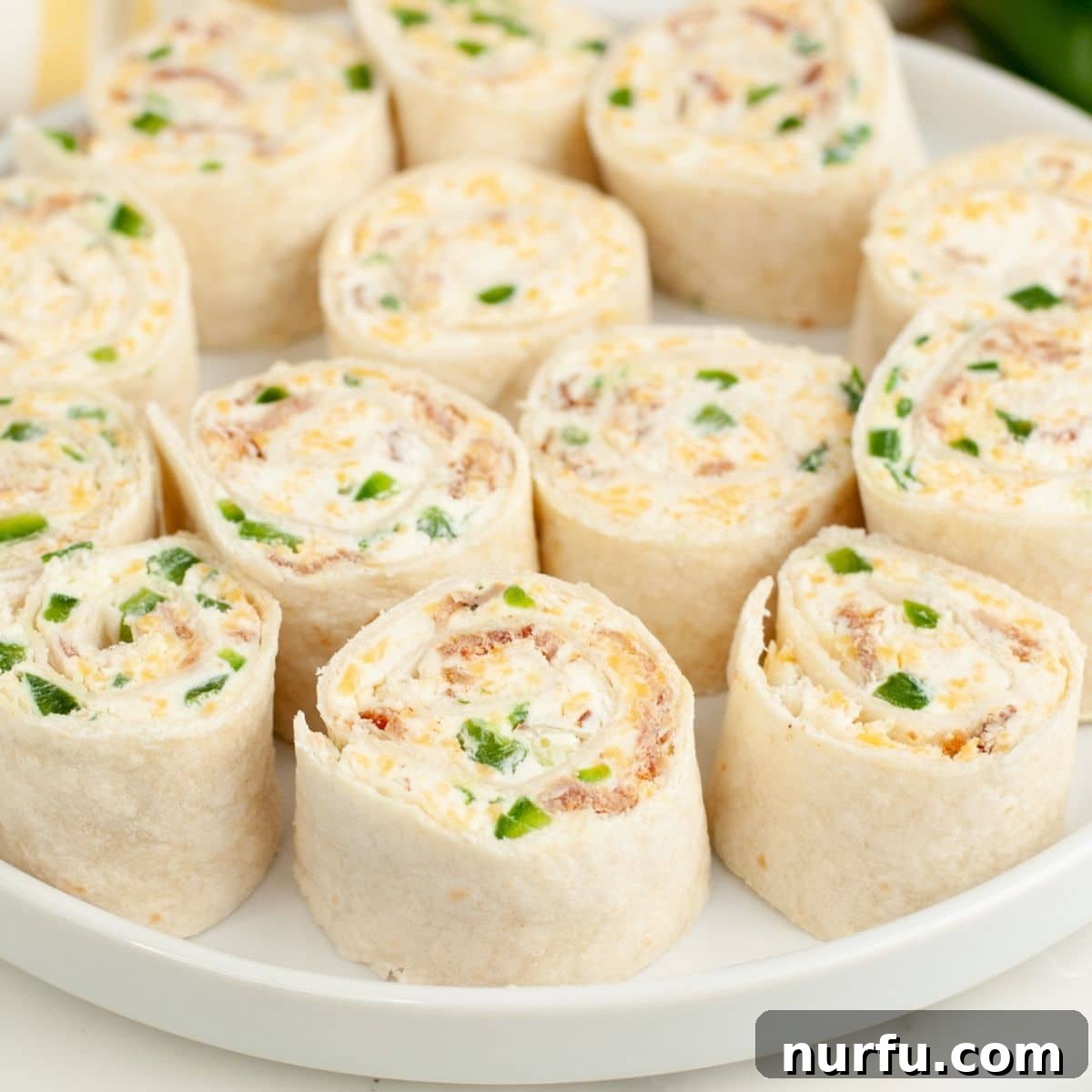 Cheesy Jalapeno Swirls 2 A vibrant plate filled with perfectly sliced Jalapeño Popper Pinwheels, showcasing their colorful layers of cream cheese, bacon, and fresh jalapeños.
