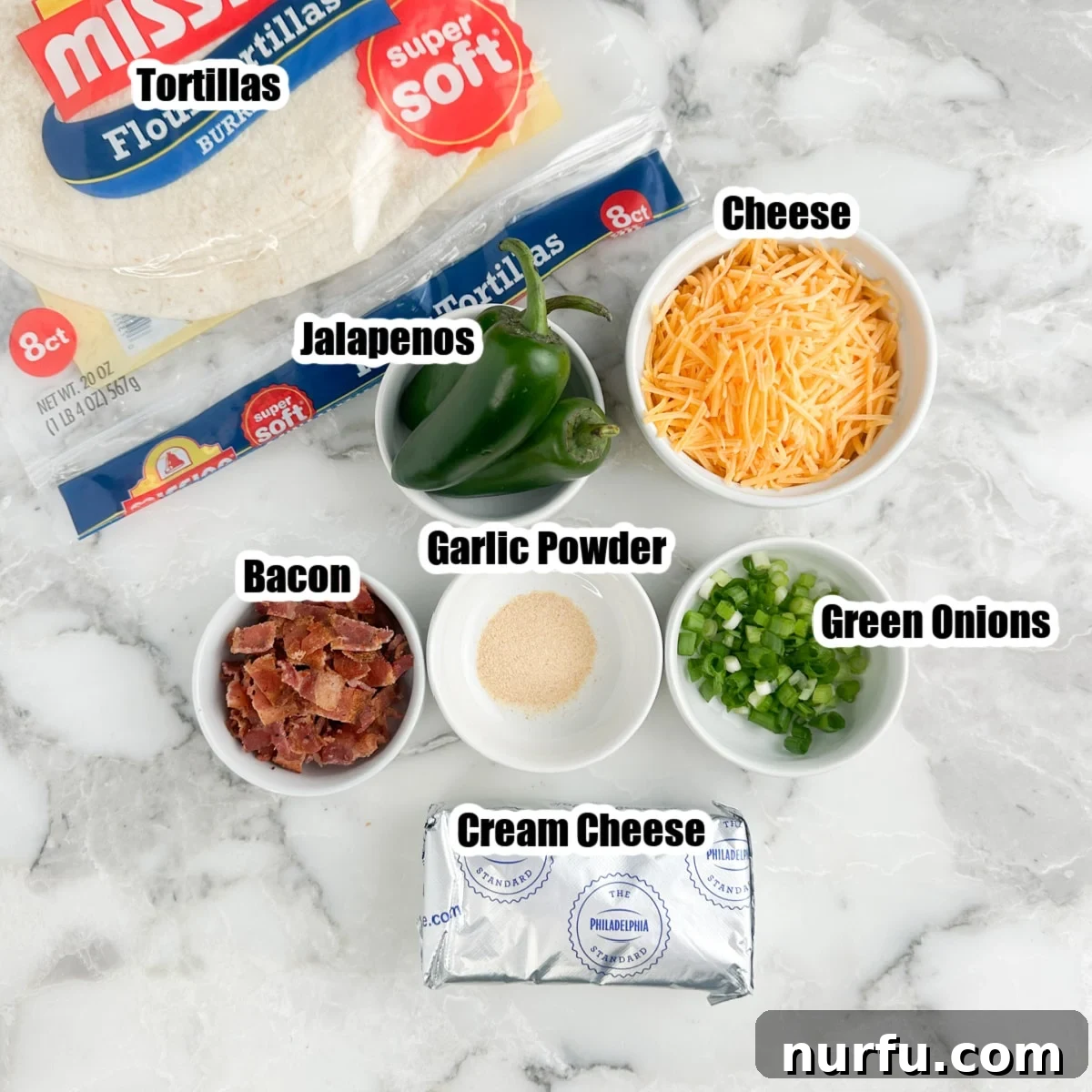 Cheesy Jalapeno Swirls 3 A flat lay photograph of all the ingredients needed for Jalapeño Popper Pinwheels: large flour tortillas, a block of softened cream cheese, a bowl of shredded cheddar cheese, fresh diced jalapeños, crispy cooked bacon crumbles, and thinly sliced green onions.