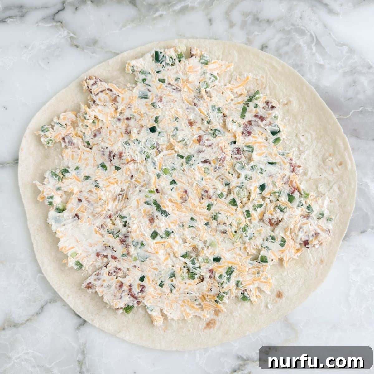 Cheesy Jalapeno Swirls 6 A large flour tortilla laid flat on a cutting board, generously covered with an even layer of the creamy jalapeño popper filling, ready for rolling.