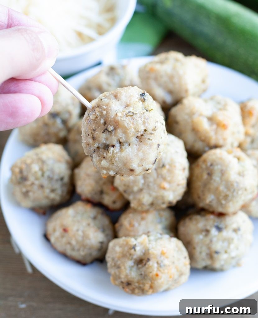 A single Parmesan Pesto Chicken Meatball pierced with a toothpick, ready to be eaten.