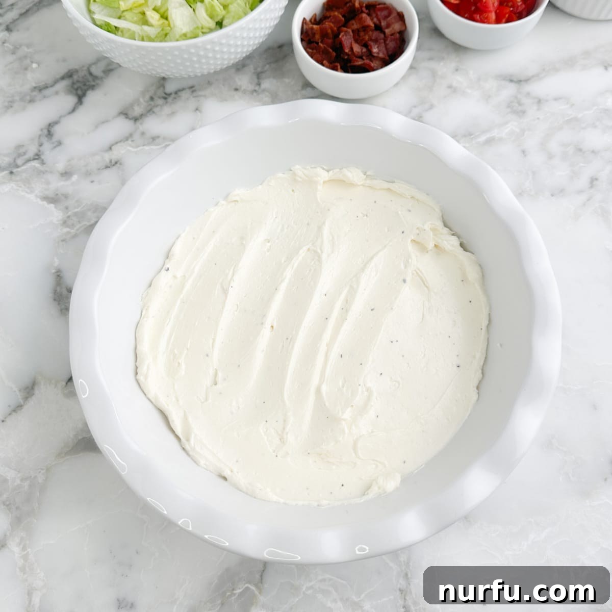 Serving dish with cream cheese and mayonnaise base spread evenly on the bottom. 