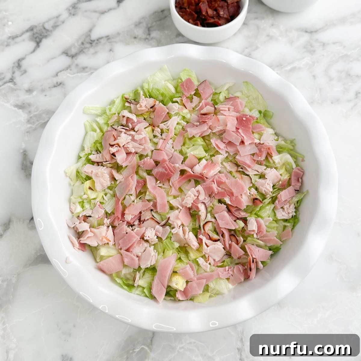 Serving dish with cream cheese, lettuce, and layers of chopped turkey and ham.