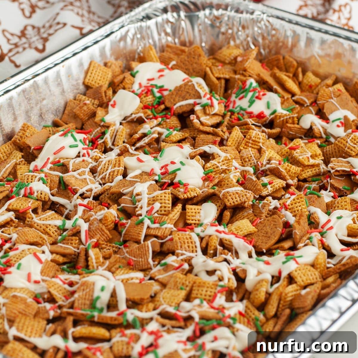Gingerbread Holiday Crunch 7 A pan of completed Gingerbread Chex Mix, beautifully drizzled with melted white chocolate and adorned with colorful holiday sprinkles, showcasing a delightful festive presentation.