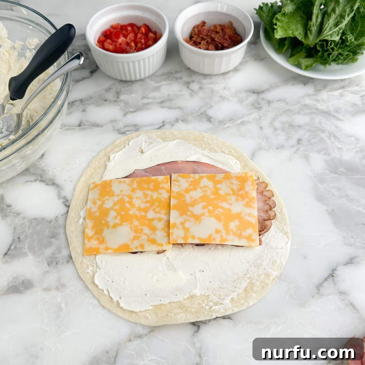 Clubhouse Pinwheel Bites 5 A tortilla with a cream cheese base, neatly topped with two slices of deli turkey, two slices of deli ham, and two slices of Colby Jack cheese laid down the center.