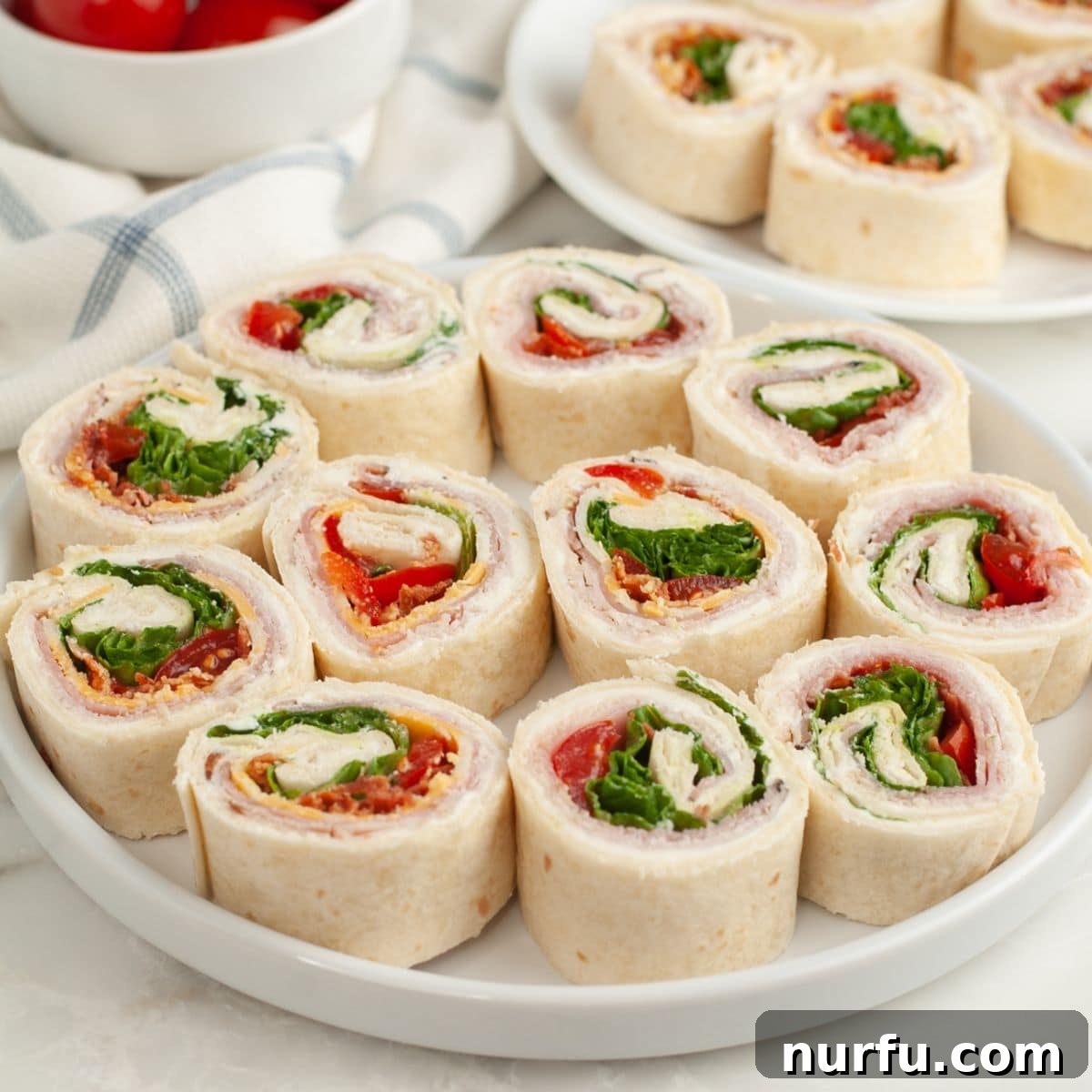 Clubhouse Pinwheel Bites 9 A beautifully arranged plate of freshly sliced club sandwich pinwheels, showcasing their vibrant layers and inviting appeal.