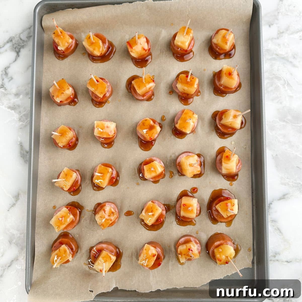 Golden Pineapple Kielbasa Poppers 7 Freshly baked pineapple kielbasa bites on a baking sheet, glistening with glaze.