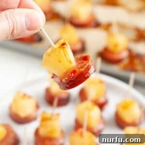 Hand holding a pineapple kielbasa bite, showcasing the sweet and savory appetizer.