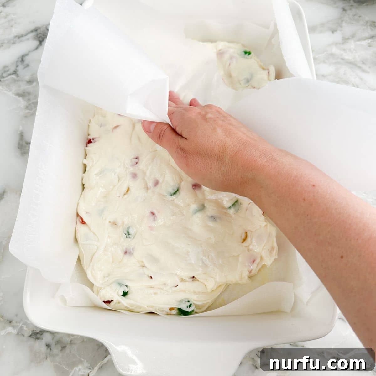 Gumdrop Nougat Cloud 6 A hand gently pressing down the warm, sticky nougat candy into a baking dish lined with parchment paper to ensure an even layer.