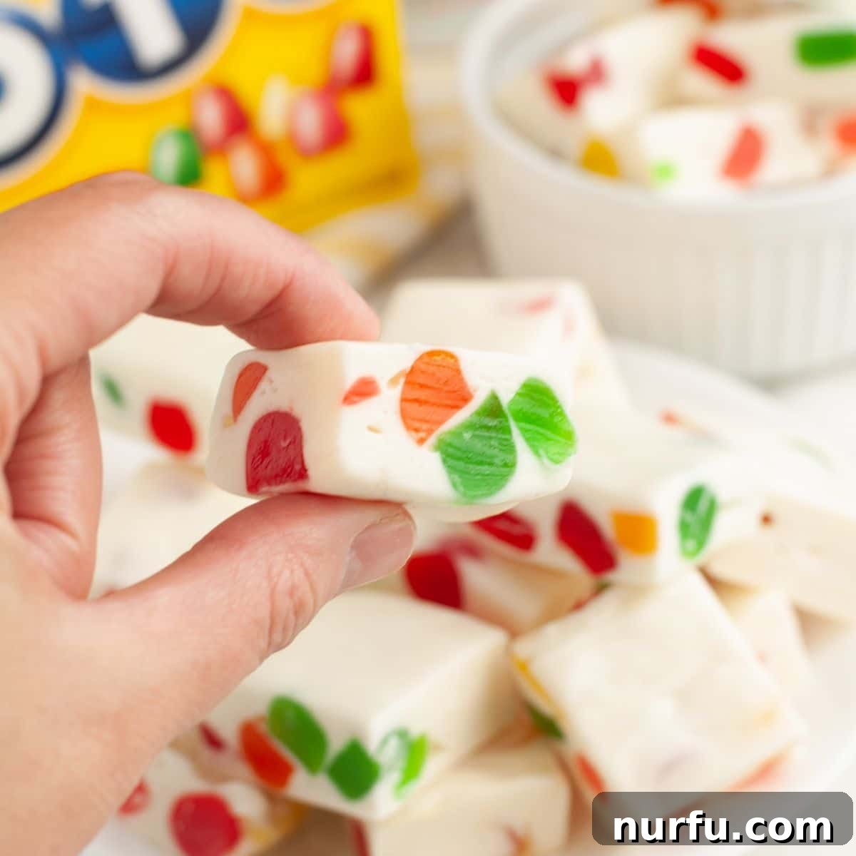 Gumdrop Nougat Cloud 8 A hand holds a single piece of vibrant gumdrop nougat candy, showcasing its soft texture and colorful inclusions.