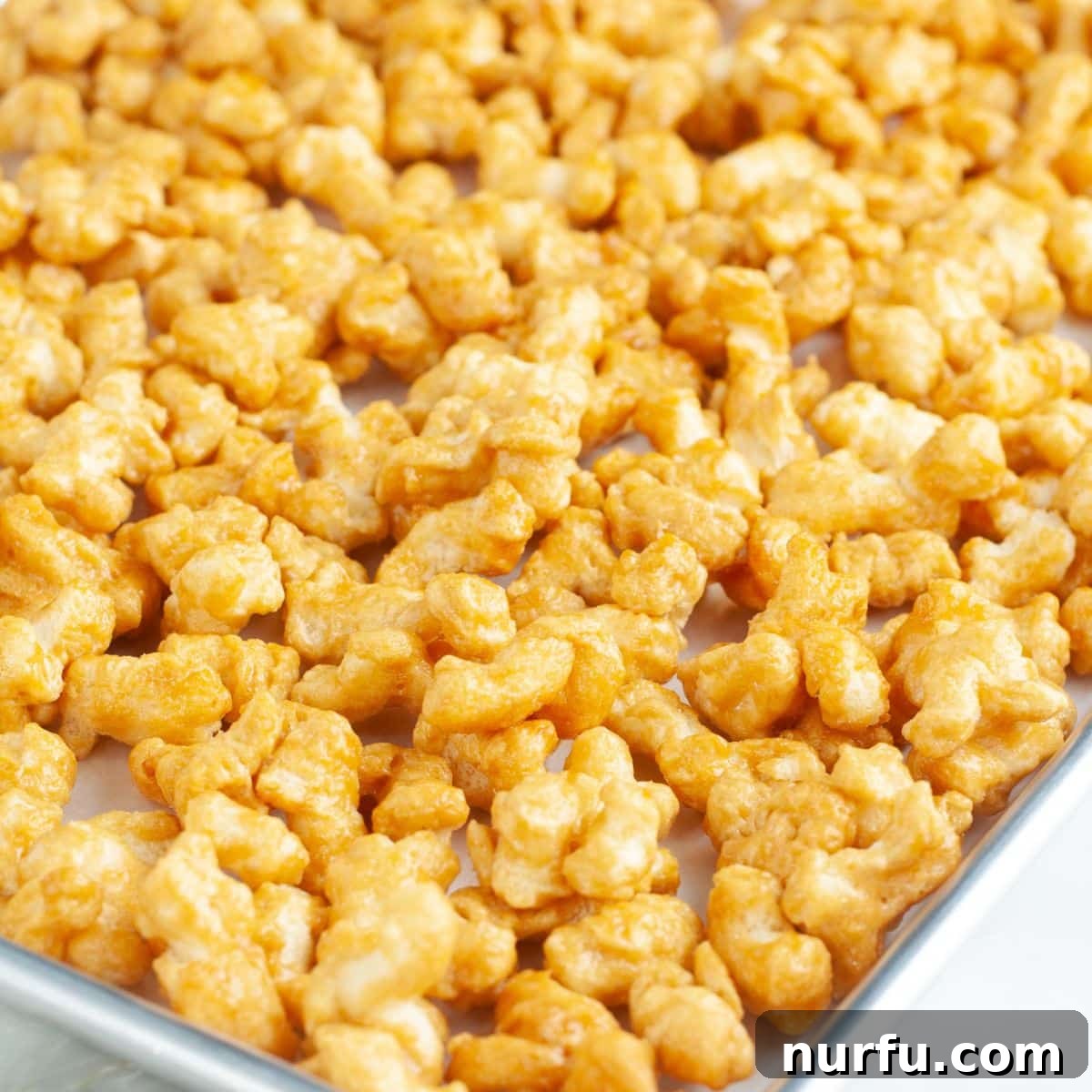 Golden Caramel Clouds 8 A close-up shot of golden, perfectly baked caramel puffcorn spread out on a baking pan, showing its irresistible texture.