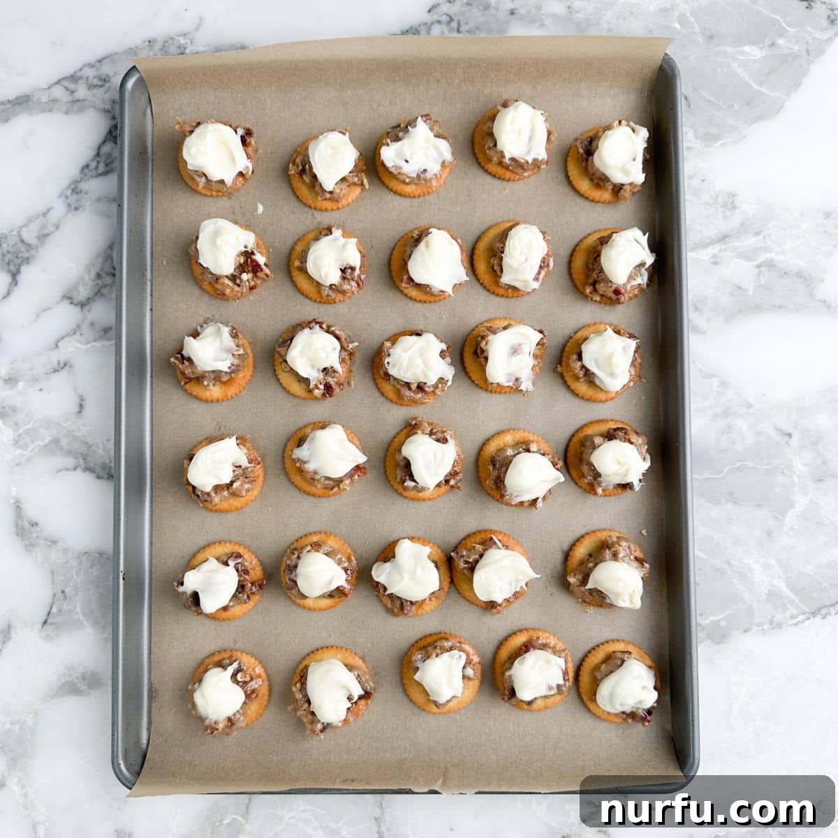 Sweet and Salty Ritz Cracker Delights 7 Baking pan with Ritz crackers generously topped with the pecan and date filling, and a dollop of cream cheese frosting.
