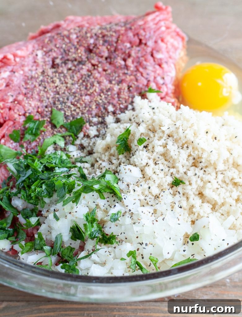 Meatball Ingredients Ready for Mixing Ground beef, fresh parsley, grated onion, Panko breadcrumbs, and an egg in a clear glass mixing bowl