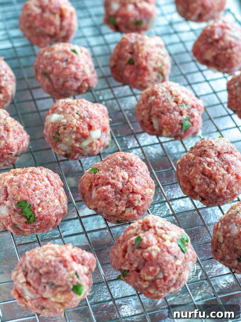 Meatballs Pre-Baking Rolled, uncooked meatballs neatly arranged on a wire rack over a baking sheet, ready for the oven