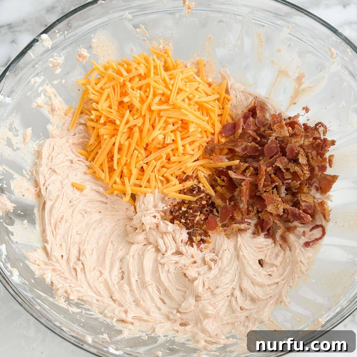 A bowl showcasing the Fire Cracker Dip mixture, with seasoned cream cheese, vibrant shredded cheese, and savory crumbled bacon expertly combined.