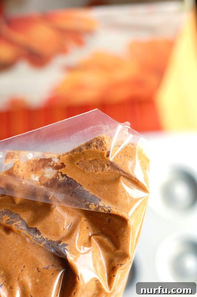 Pumpkin donut batter being piped into a greased donut pan using a Ziploc bag.