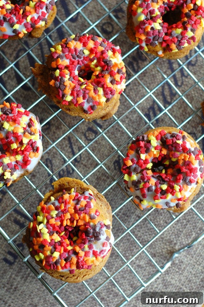 A pile of perfectly glazed and sprinkled mini pumpkin donuts, ready to be served.