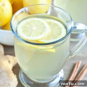 A glass coffee cup filled with amber ginger tea and a slice of lemon.