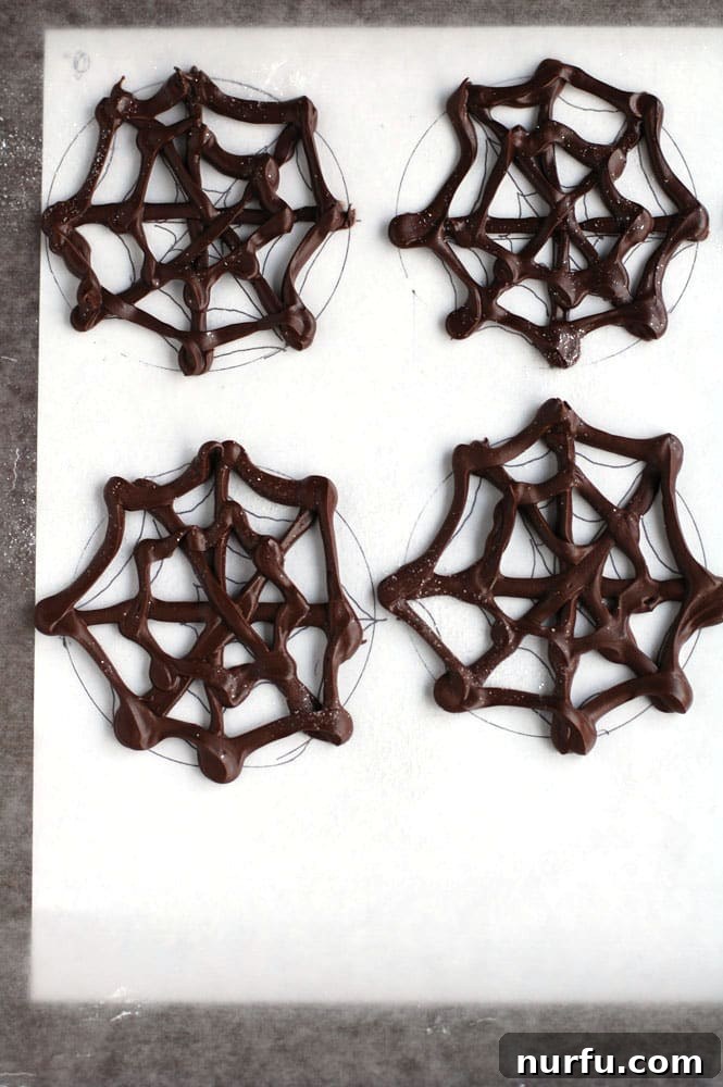 Hardened Chocolate Spider Web Toppers Delicate chocolate spider web toppers, some embellished with edible glitter, in the process of hardening on wax paper