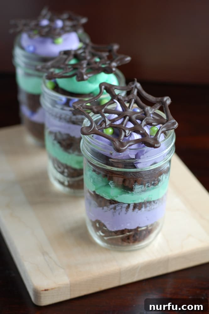 Halloween Mason Jar Cakes Display A collection of decorated Halloween Mason Jar Cakes with colorful frosting and chocolate spider webs, showcasing their festive appeal