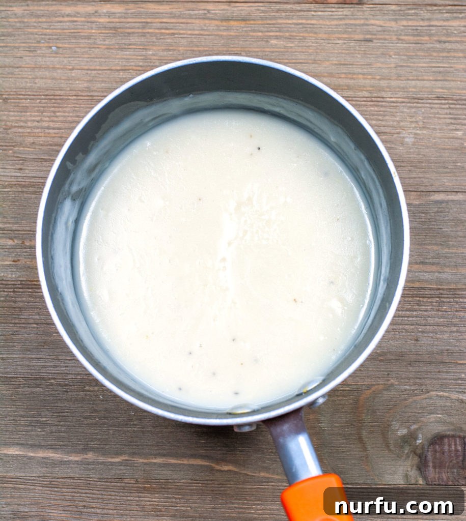 Rich, homemade cream sauce simmering gently, ready to transform into Crockpot Chicken and Noodles.