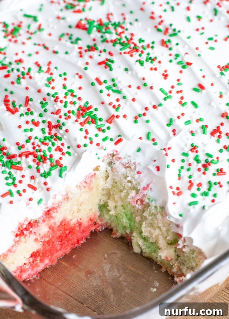 Holiday Jello Cake Slice A slice of Holiday Jello Cake, showing distinct red and green layers with whipped topping and sprinkles.