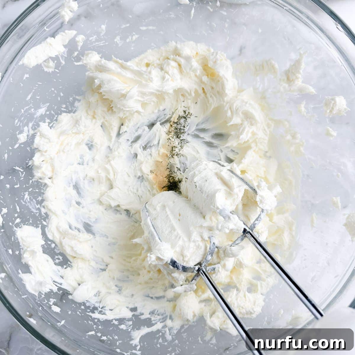 Close-up of a bowl with whipped cream cheese, showing its creamy texture after being mixed.