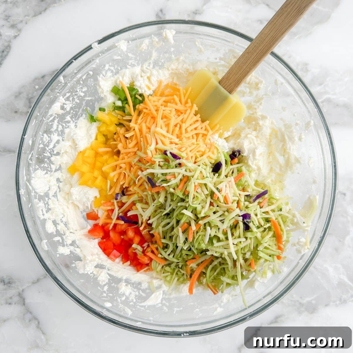 Bowl of cream cheese mixed with colorful chopped vegetables like bell peppers, green onions, broccoli slaw, and shredded cheese.
