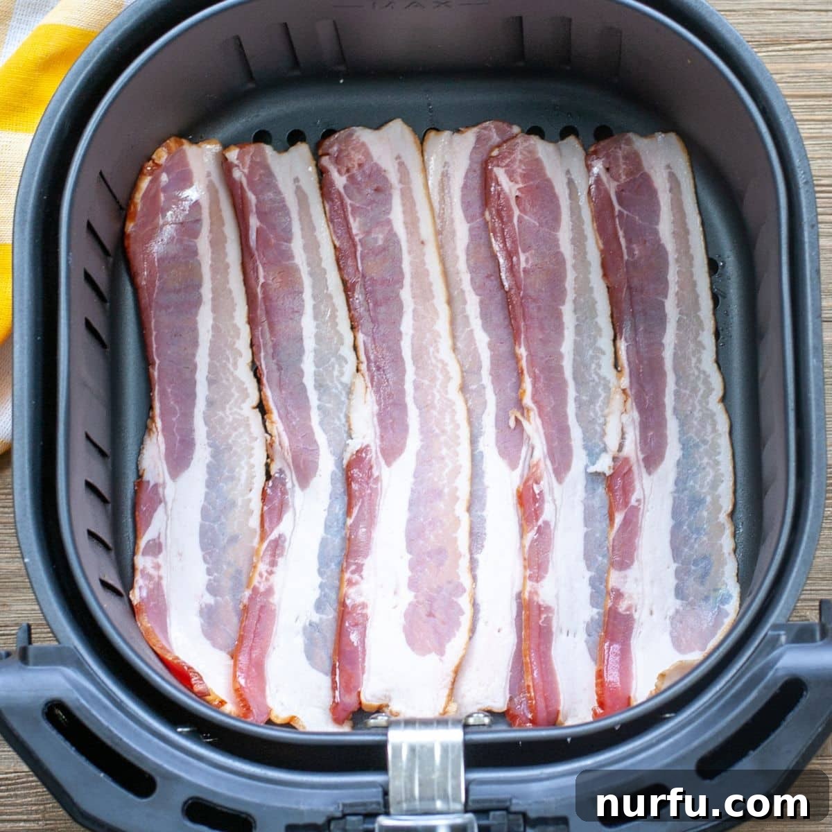 Crispy Air Fryer Bacon 2 Raw, uncooked bacon strips neatly arranged in a single layer inside an air fryer basket, ready for cooking.