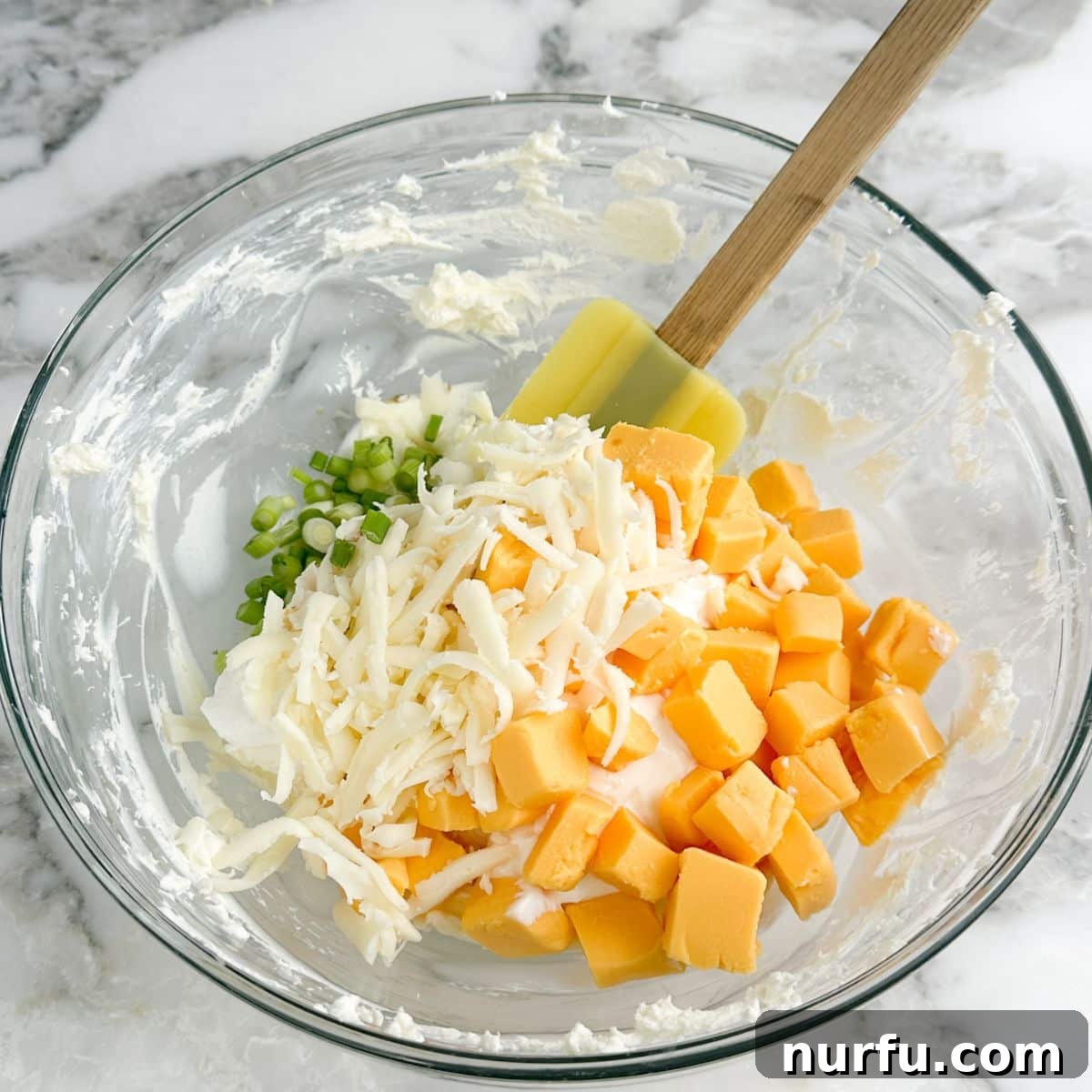 Whisker Rage Plunge 4 A bowl containing softened cream cheese, cubed Velveeta, shredded Monterey Jack, and diced green onions, ready to be mixed.