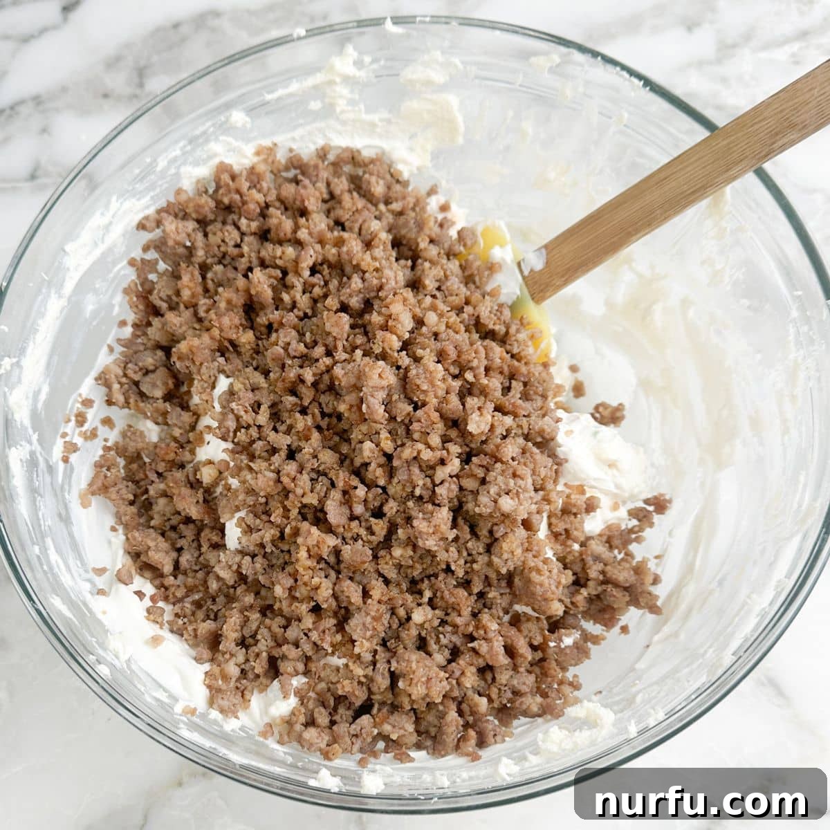 Whisker Rage Plunge 6 A mixing bowl filled with the creamy cheese base and crumbled, cooked sausage, ready to be stirred together.