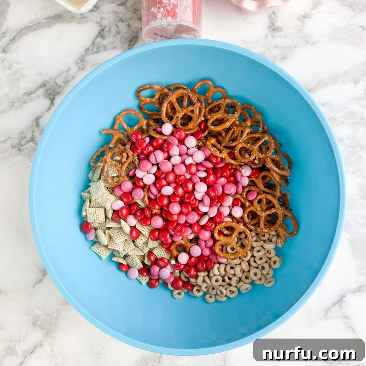 Blue bowl with pretzels, M&M'x, Cheerios, and Chex. 