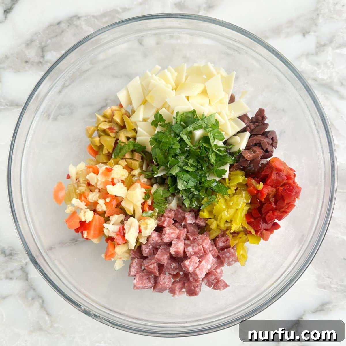 New Orleans Muffuletta Party Dip 4 A large mixing bowl filled with finely diced salami, provolone cheese, colorful olives, peppers, and fresh parsley, all prepped for the muffuletta dip.