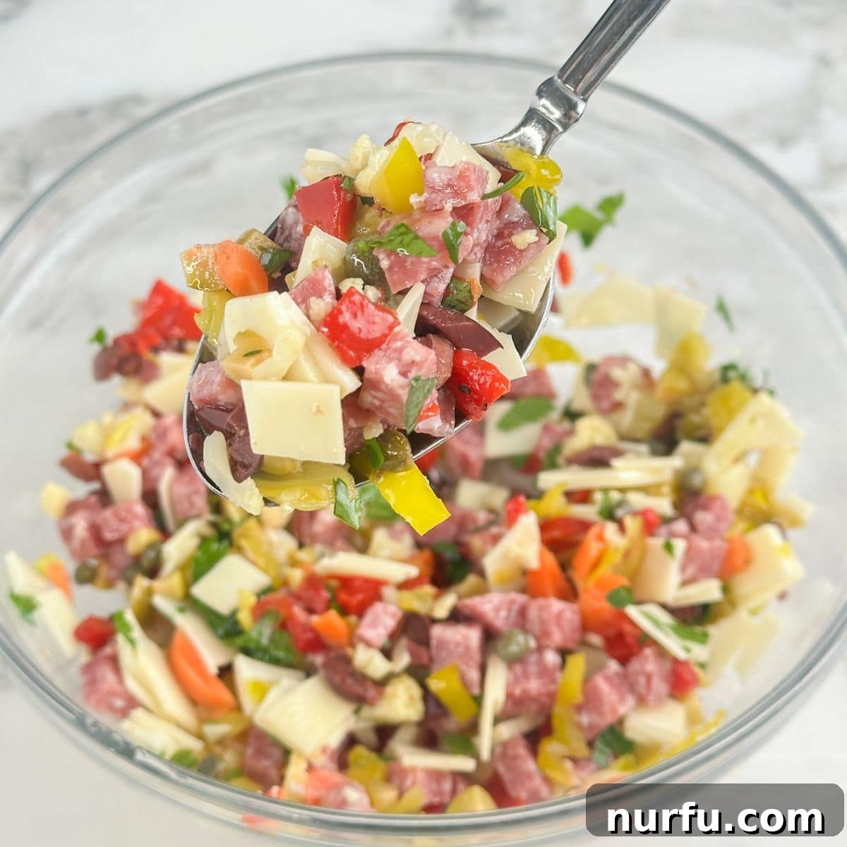New Orleans Muffuletta Party Dip 5 A large bowl of thoroughly mixed muffuletta dip, with a serving spoon nestled inside, ready to be enjoyed.
