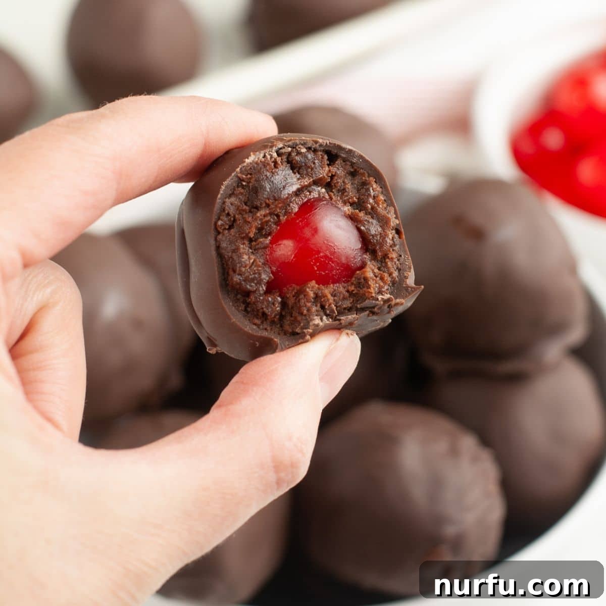 Irresistible Chocolate Cherry Brownie Bites 2 A hand holding a perfectly round, chocolate-covered cherry brownie bite, showcasing its smooth chocolate coating.