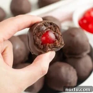 Irresistible Chocolate Cherry Brownie Bites 13 A hand holding a perfectly round, chocolate-covered cherry brownie bite, showcasing its smooth chocolate coating.