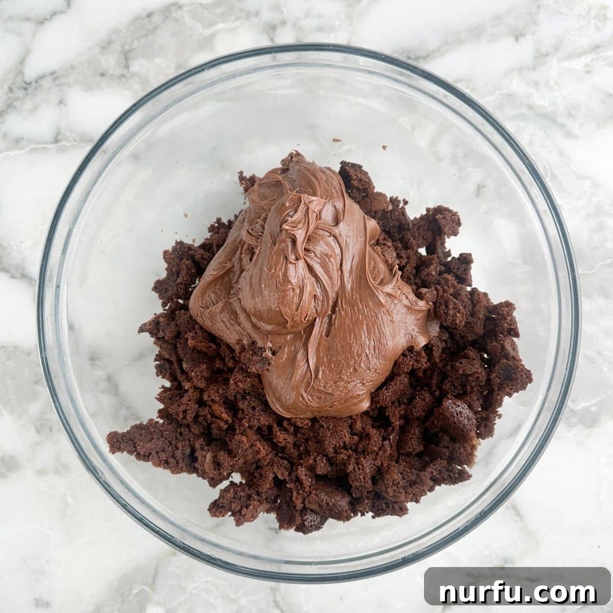 Irresistible Chocolate Cherry Brownie Bites 5 A bowl filled with crumbled brownies and a scoop of chocolate frosting, ready to be mixed.