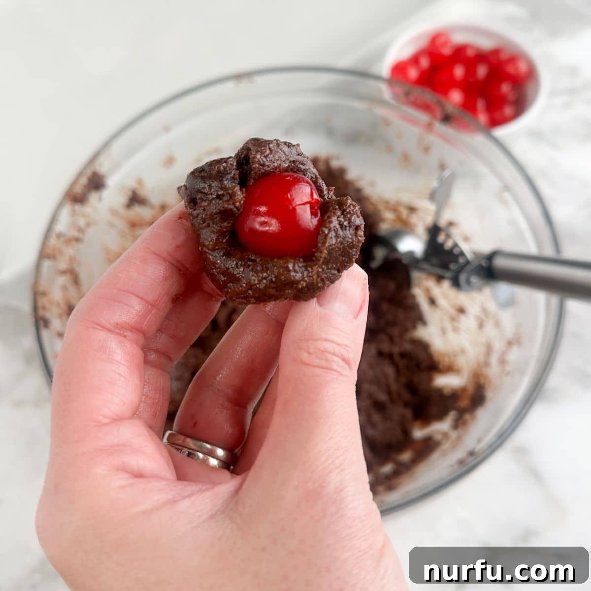 Irresistible Chocolate Cherry Brownie Bites 7 A hand holding a ball of brownie mixture with a single maraschino cherry nestled in its center.
