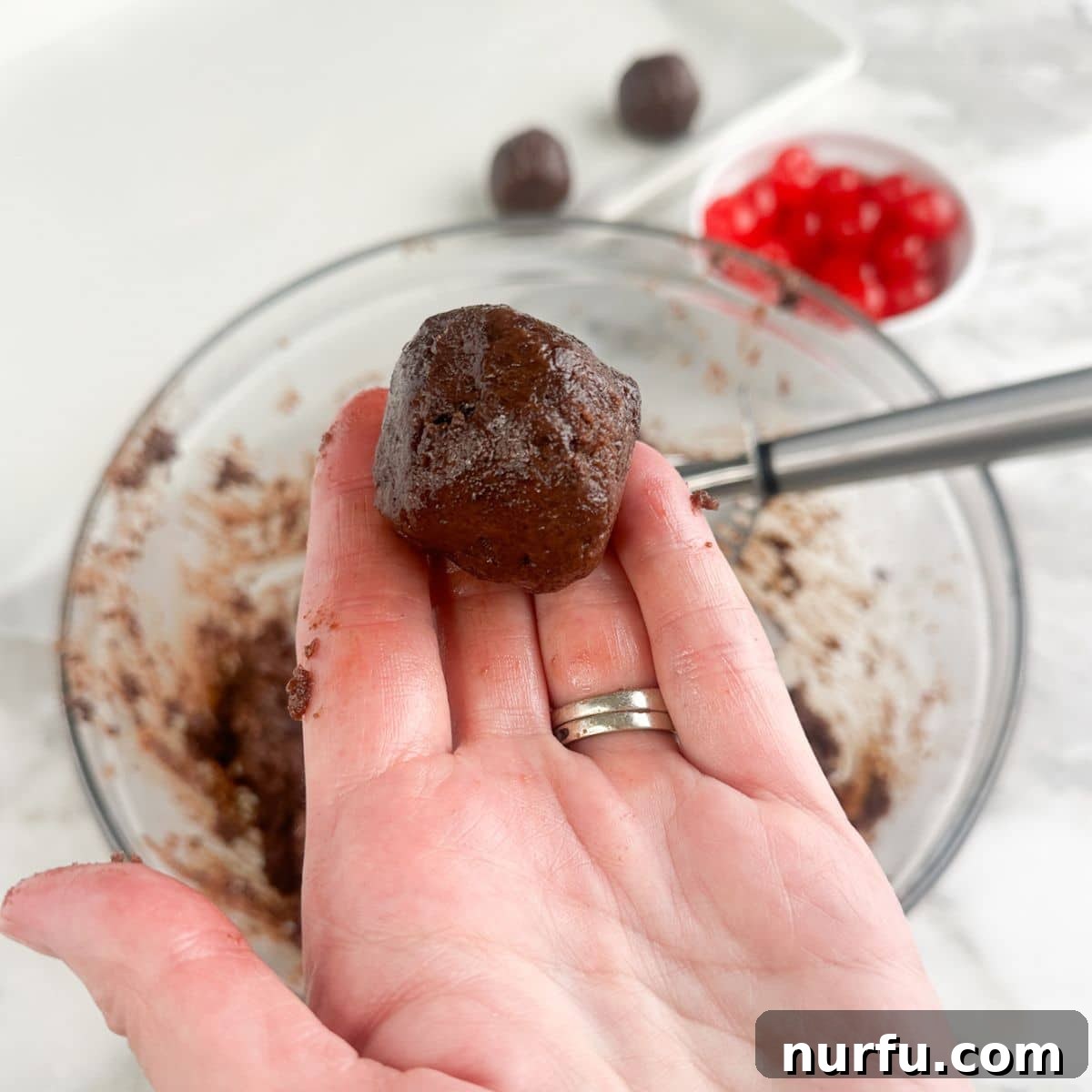 Irresistible Chocolate Cherry Brownie Bites 8 A hand expertly rolling the brownie mixture around a cherry to fully enclose it.
