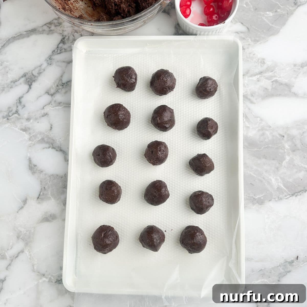 Irresistible Chocolate Cherry Brownie Bites 9 A baking sheet neatly arranged with numerous un-coated brownie bomb bites, ready for freezing.