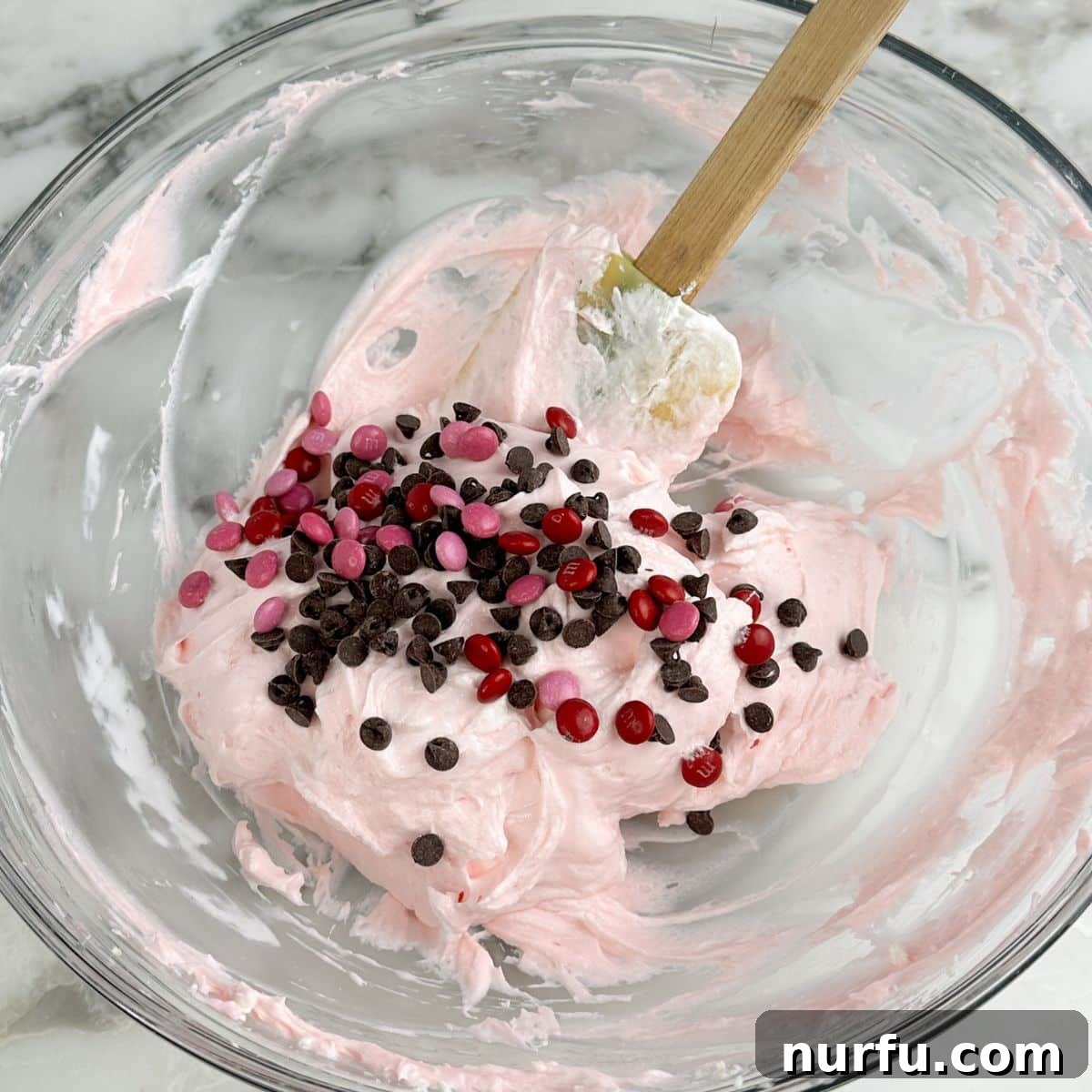 Pink Party Dip 6 A close-up shot of the finished pink dessert dip, generously studded with mini chocolate chips and colorful mini M&M's, showcasing its delightful mix-ins before serving.