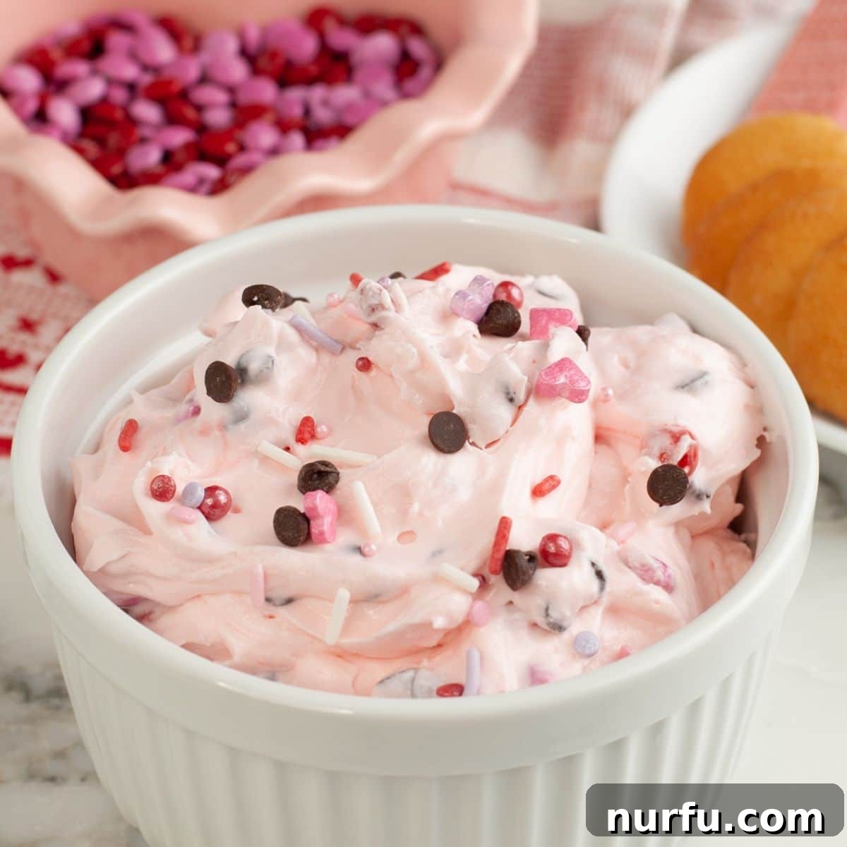 Pink Party Dip 7 A beautifully presented bowl of vibrant pink dessert dip, adorned with colorful sprinkles, sitting on a wooden surface. The focus is on the inviting texture and festive appearance of the dip.